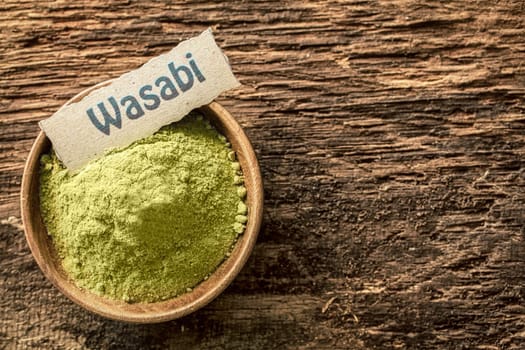 Wasabi, a pungent green Japanese condiment made from the root of the herb Eutrema wasabi, dried and powdered in a bowl standing on a textured weathered surface with copyspace