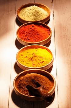 Line of colourful ground spice with four bowls of chilli powder,red cayenne pepper, curry and ground green tea on wooden boards