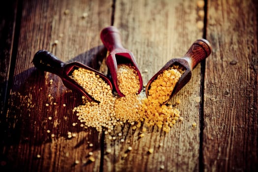 Uncooked edible cereal grains in three wooden scoops on an old aged wooden background of textured boards, high angle view