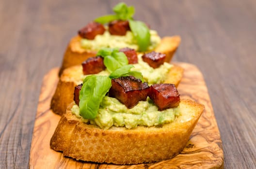 Bruschetta with avocado,chorizo sausage and basil on a wooden board