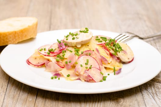 Potato salad with sausage,radish and chives on a white plate