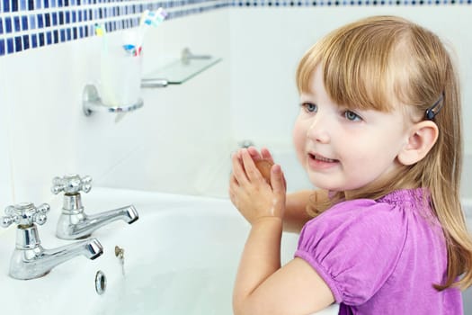 a young child washing her hands in a bathroom sink