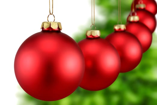 Red Christmas baubles hang in a row in front of a Christmas tree