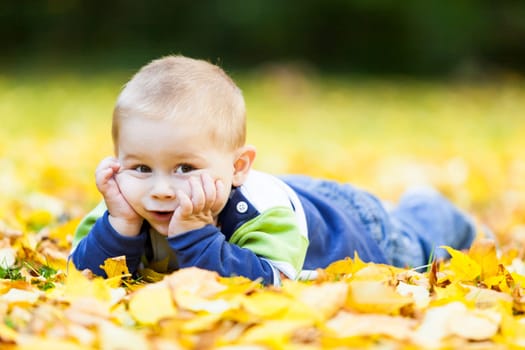 little boy lying on the yellow leaves in the autumn park
