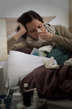 Sick woman with flu sneezing blowing her nose in bed