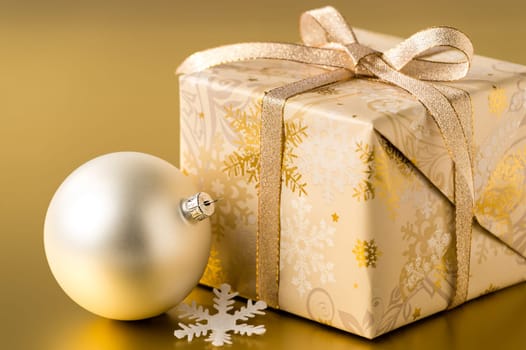 Christmas present and silver bauble on gold background
