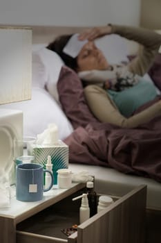 Flu medicines on bedside table beside ill woman in bed