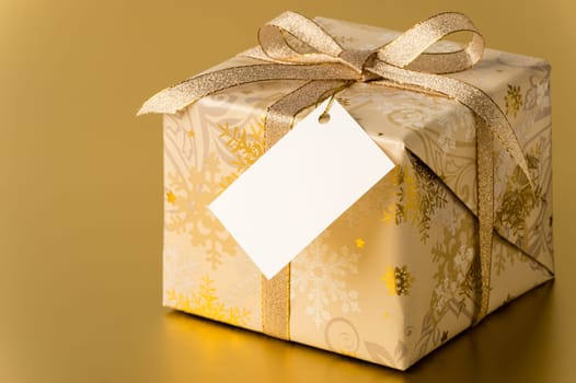 Christmas present with ribbon and blank tag on gold background copyspace