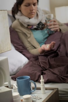 Ill woman lying in bedroom with cold flu medicine pills