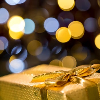 Christmas gift with sparkling lights background wrapped in gold paper