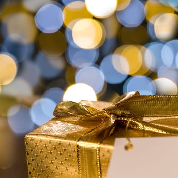 Golden Christmas gift with label sparkling lights on background