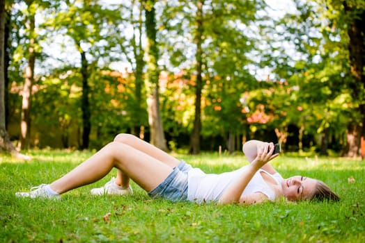 Mobility - teen girl lying on grass and working with smartphone