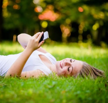 Mobility - teen girl lying on grass and working with smartphone