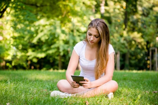 Young woman (teen girl) reading book on electronic book reader - outdoor in nature