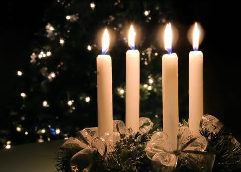 Christmas advent wreath with burning candles. Lights on x-mas tree in background