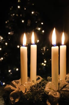 Christmas advent wreath with burning candles. Lights on x-mas tree in background