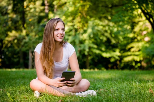 Young woman (teen girl) reading book on electronic book reader - outdoor in nature