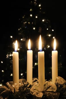 Christmas advent wreath with burning candles. Lights on x-mas tree in background