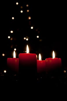 Christmas advent wreath with red burning candles. Lights on x-mas tree in background