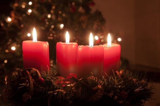 Christmas advent wreath with red burning candles. Lights on x-mas tree in background