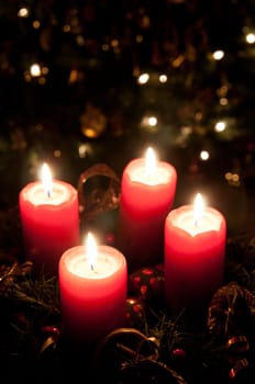 Christmas advent wreath with red burning candles. Lights on x-mas tree in background