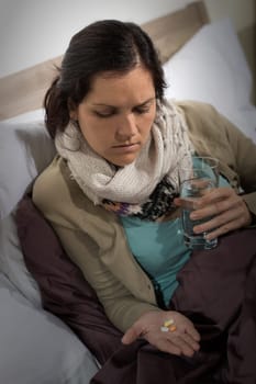 Sick woman holding and looking at medicine pills flu cold