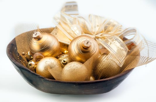 Colourful shiny collection of golden Christmas baubles, bows and ribbons in a wooden bowl over a white background