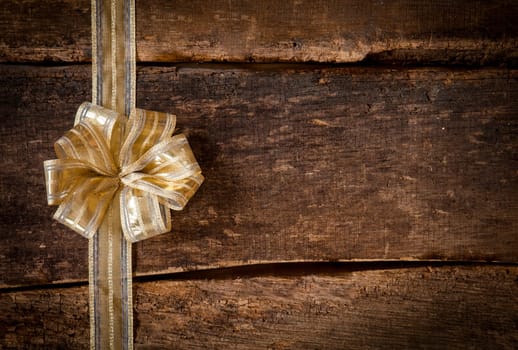Festive gold ribbon and bow border to the left of the frame over a grunge dark textured rustic wood background with copyspace for your Christmas, anniversary or birthday wishes or invitation