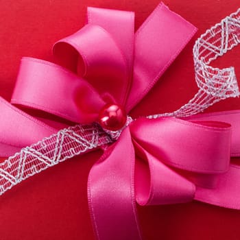 Ornamental red or scarlet bow with filigree white braid fastened in the centre with a pearl for decorating festive Christmas, Valentines, birthday or anniversary packaging