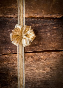 Pretty ornamental gold bow and ribbon over dark textured wooden planks with copyspace for your text or Christmas, anniversary or birthday greeting