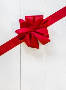 Decorative red bow and ribbon on rustic white painted wooden boards with copyspace for your Christmas or Valentines greeting