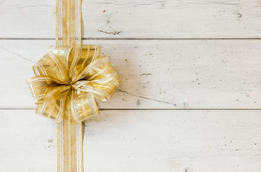 Metallic gold decorative Christmas bow forming a border on the left on a background of rustic white painted wooden planks with copyspace for your seasonal greeting