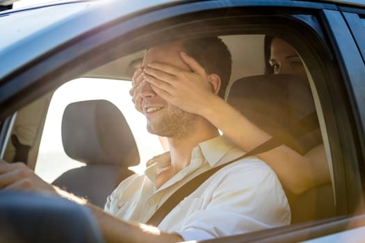 Young couple in car - woman covering eyes of her boyfriend