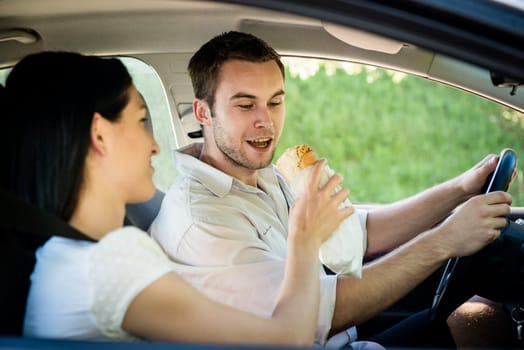 Couple in car - man is driving and woman is feeding him