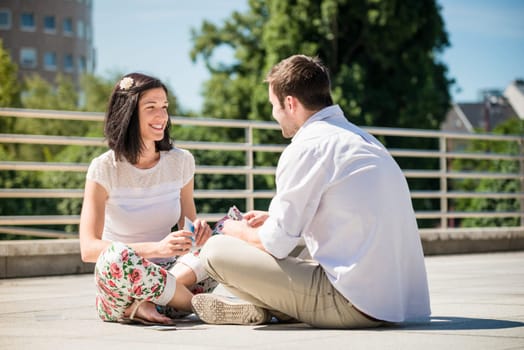 Young couple playing cards outdoor sitting on ground