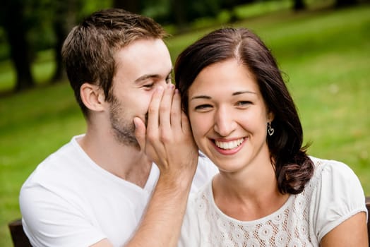 Young man whispering to woman (girlfriend) - outdoor lifestyle photo
