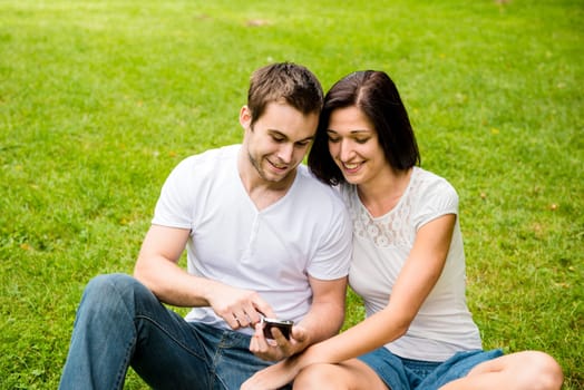 Young happy couple looking on mobile phone - outdooor in nature