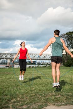 Young fitness couple exercising outdoor - jumping with skipping rope