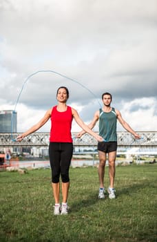 Young fitness couple exercising outdoor - jumping with skipping rope