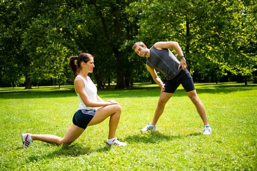 Young man and woman exercising and stretching muscles before sport activity - outdoor in nature