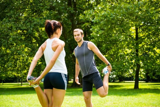 Young couple exercising and stretching muscles before sport activity - outdoor in nature
