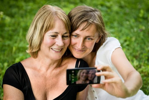 Adult daughter and her senior mother are taking picture with mobile phone