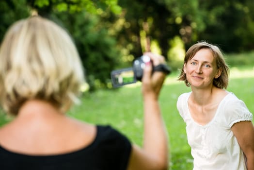 Senior mother is taking video of her adult daughter in nature with camcorder