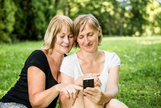 Senior mother showing on mobile phone to her adult child - outdoor in nature