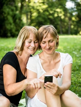 Mature mother showing on mobile phone to her adult child - outdoor in nature