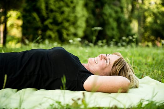 Smiling attractive senior woman lying outdoor on rug in nature