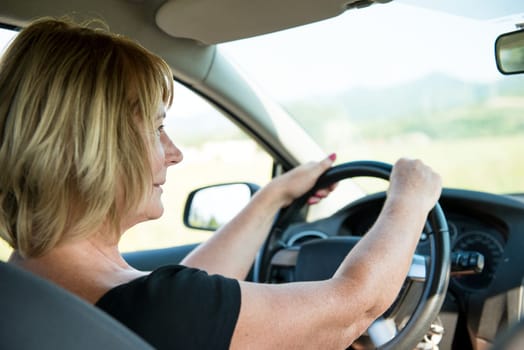 Lifestyle photo of attractive mature woman driving car