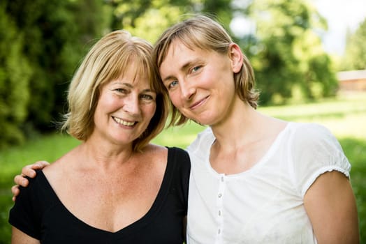 Outdoor portrait of smiling happy senior mother with her adult daughter