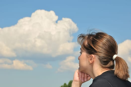Head of Young woman dreaming in day with blue sky and white clouds in background - detail