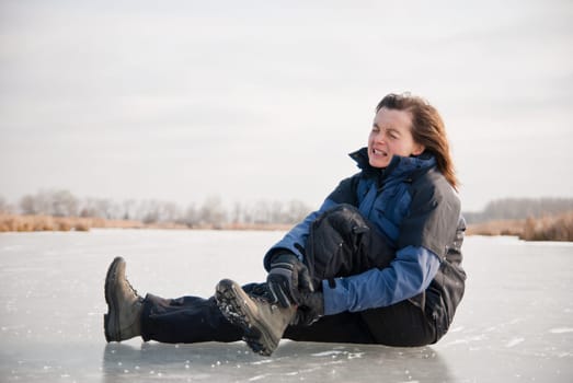 Young woman with ankle injury on frozen icy lake